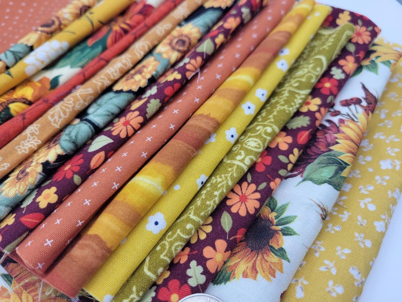 Op de afbeelding: Een verzameling stofresten met verschillende herfstpatronen, waaronder zonnebloemen, bladeren en paisley-patronen in tinten geel, oranje, bruin en bordeaux.