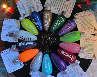May include: A collection of twelve glitter-filled, lightbulb-shaped ornaments arranged in a circle. Each ornament features a silver cap and a printed name or title, including Billy, Friend, Connor, Melissa, and Teacher, paired with individual gift tags.