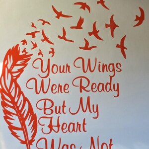 Op de afbeelding: Een rode vinyl sticker met een grote veer aan de linkerkant die overgaat in een zwerm kleine vogels die omhoog vliegen. De tekst "Your Wings Were Ready But My Heart Was Not" staat in een cursief lettertype in het midden.