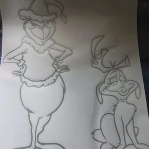 May include: A black and white line drawing on a white surface featuring two characters. On the left, a tall, slender creature wears a Santa hat and a fur-trimmed outfit. On the right, a smaller, four-legged creature with antlers sits upright.