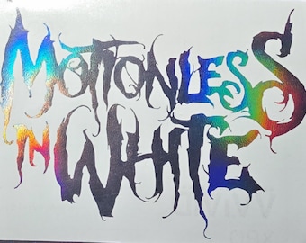May include: A holographic sticker featuring the text Motionless In White written in a jagged, stylized font. The lettering displays a shifting spectrum of iridescent colors including blue, purple, green, and orange against a plain white background.