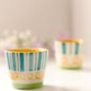 A vibrant set of 2 hand-painted ceramic shot glasses/espresso cups, each holding 75ml, with colorful designs, placed among fresh flowers, perfect for elevating any barware collection.