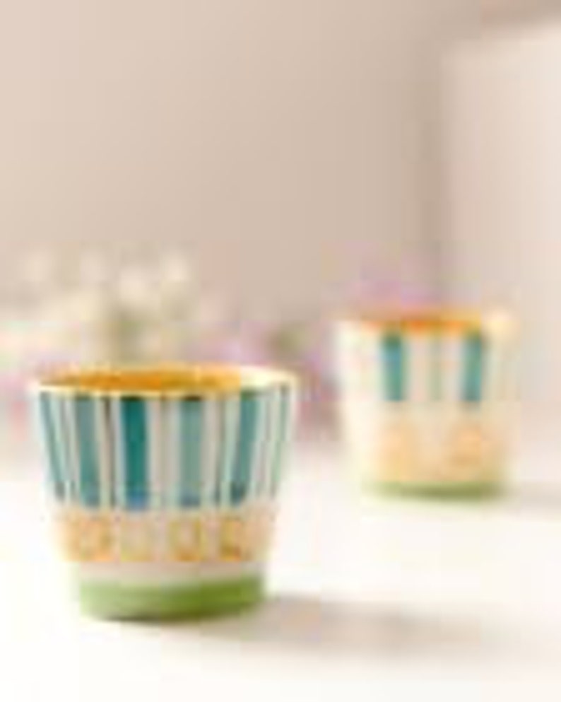 A vibrant set of 2 hand-painted ceramic shot glasses/espresso cups, each holding 75ml, with colorful designs, placed among fresh flowers, perfect for elevating any barware collection.