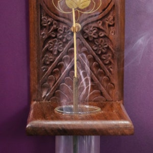 May include: A wooden incense holder with intricate carvings and a single incense stick burning inside. Smoke rises from the stick, creating a wispy, ethereal effect.
