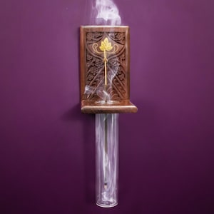 May include: A wooden incense holder with intricate carvings and a glass tube for burning incense sticks. Smoke rises from the tube, creating a wispy, ethereal effect.
