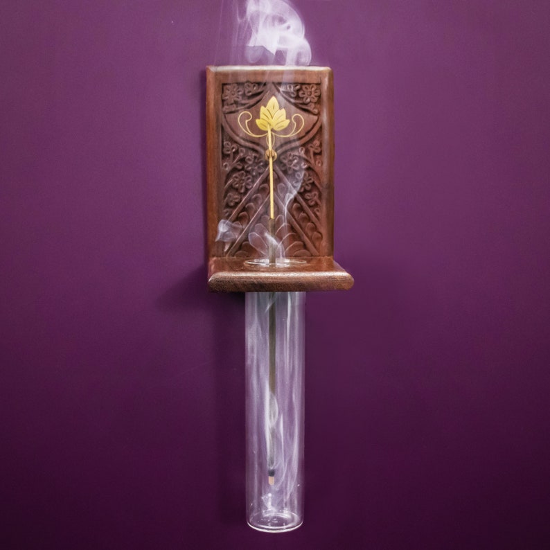 May include: A wooden incense holder with intricate carvings and a glass tube for burning incense sticks. Smoke rises from the tube, creating a wispy, ethereal effect.