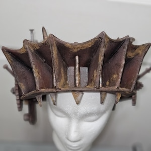 May include: A rusty brown and gold crown with spikes and gears. The crown is made of metal and has a distressed finish.