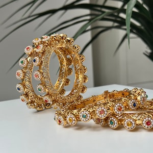 Peut inclure: Bracelets dorés ornés de filigranes complexes et d'accents de pierres précieuses colorées. Les bracelets présentent un motif floral et sont ornés de petites perles. Un ensemble de bijoux pour les occasions spéciales.