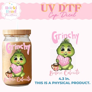 May include: A green Grinch character holding a pink heart-shaped pastry and a cup of coffee. The text "Grinchy Before Cafecito" is written below the character. The image is a UV DTF cup decal, 4.3 inches in size.