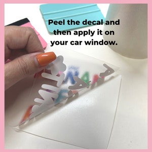 May include: A hand peeling back a clear transfer sheet to reveal a colorful vinyl decal that says "FAMILY". The decal is on a white background. The text "Peel the decal and then apply it on your car window." is visible in the image.