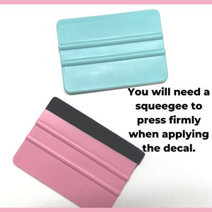May include: Two plastic squeegees, one pink and one light blue, with black handles. The squeegees have three parallel lines on the blade. The text "You will need a squeegee to press firmly when applying the decal." is below the squeegees.