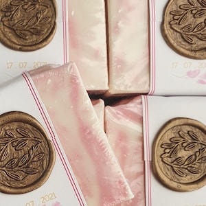 Puede incluir: Cuatro barras de jabón envueltas en papel blanco con sellos de cera dorada. Los sellos tienen un diseño floral y el texto "17 07 2021" y "07 2021".