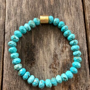 May include: Turquoise gemstone bracelet with a gold bead accent. The bracelet is made of faceted turquoise beads and has a simple, elegant design.