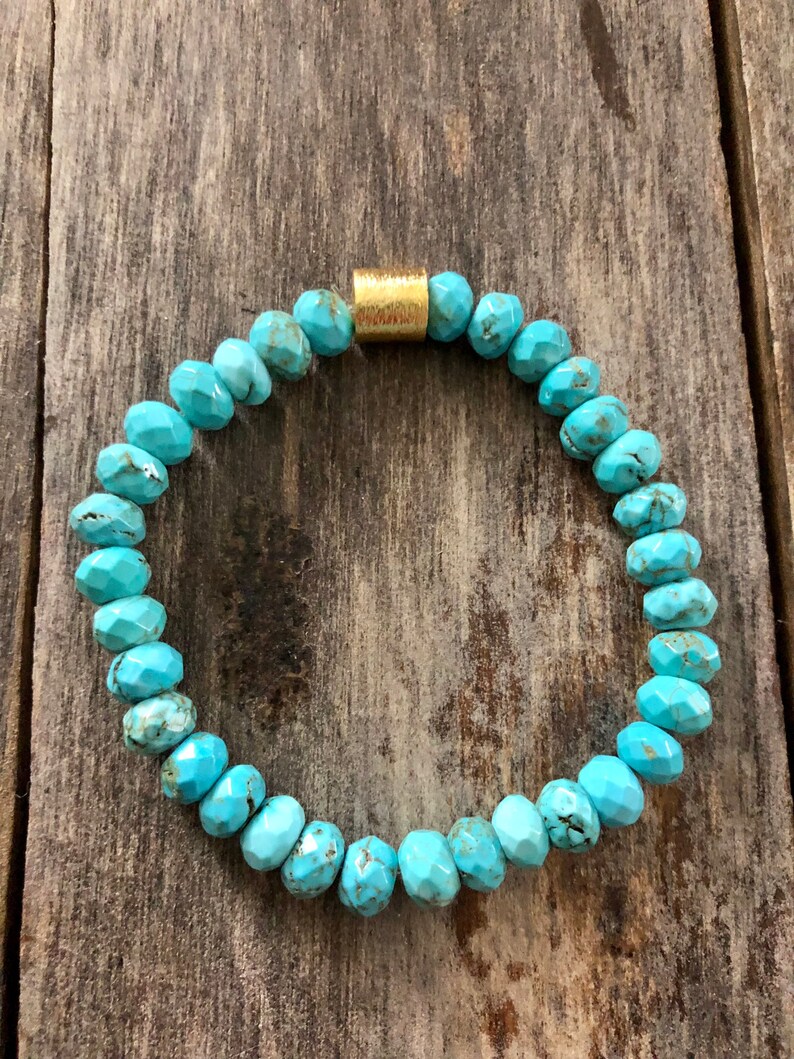 May include: Turquoise gemstone bracelet with a gold bead accent. The bracelet is made of faceted turquoise beads and has a simple, elegant design.