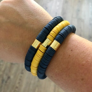 May include: Three stacked bracelets with black and yellow beads. The beads are round and have a matte finish. The bracelet has a gold accent.