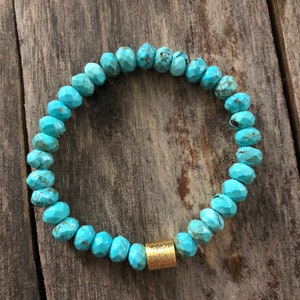May include: Turquoise gemstone bracelet with a gold bead accent. The bracelet is made of faceted turquoise beads and has a simple design.