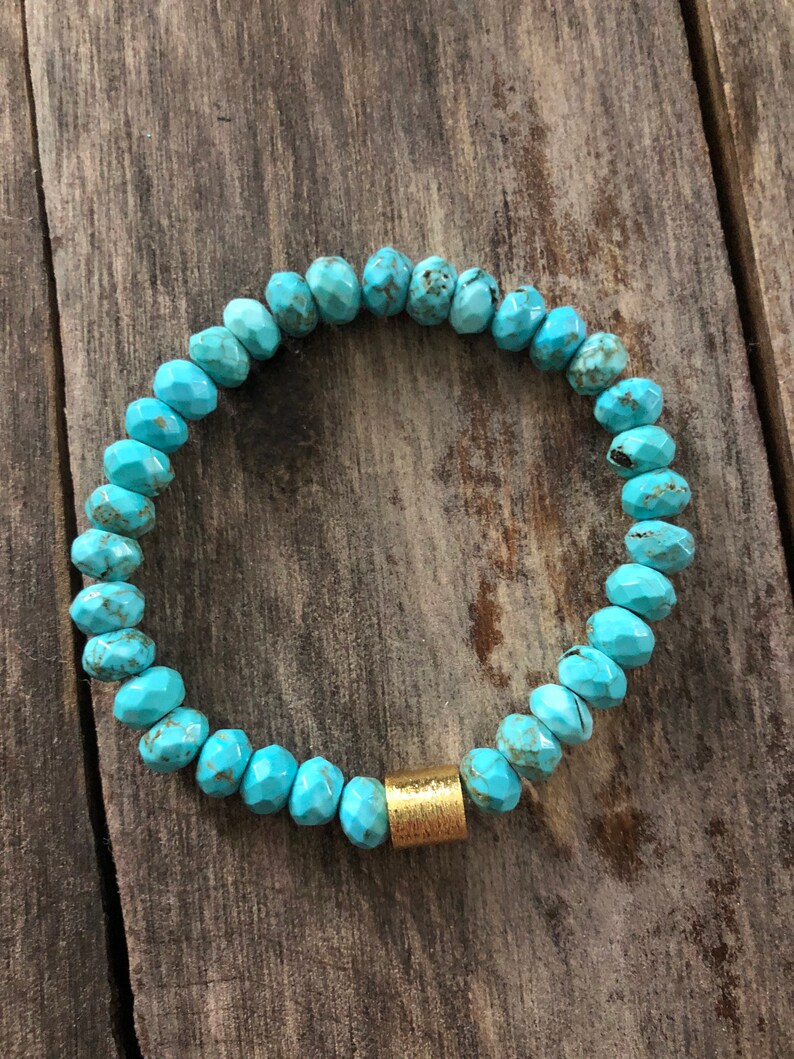 May include: Turquoise gemstone bracelet with a gold bead accent. The bracelet is made of faceted turquoise beads and has a simple design.
