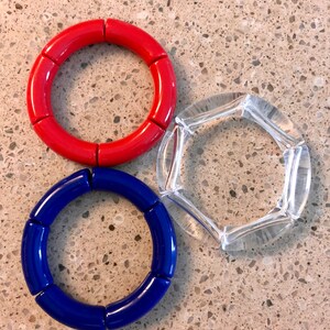 May include: Three bracelets, one red, one blue, and one clear, made of round, segmented pieces.