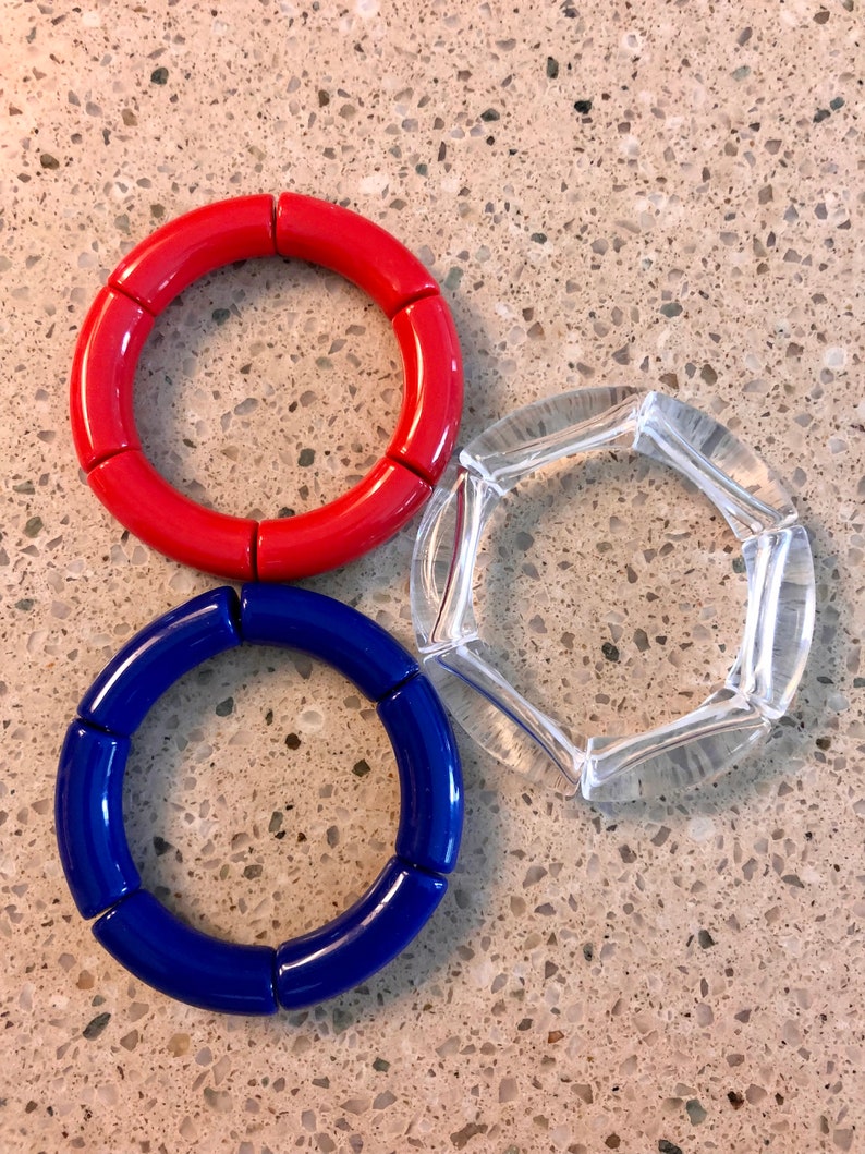 May include: Three bracelets, one red, one blue, and one clear, made of round, segmented pieces.
