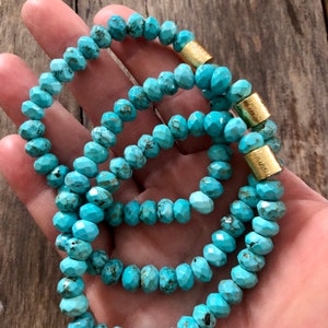 May include: Three turquoise beaded bracelets with gold accents. The beads are faceted and have a slightly irregular shape. The bracelets are stacked on top of each other.