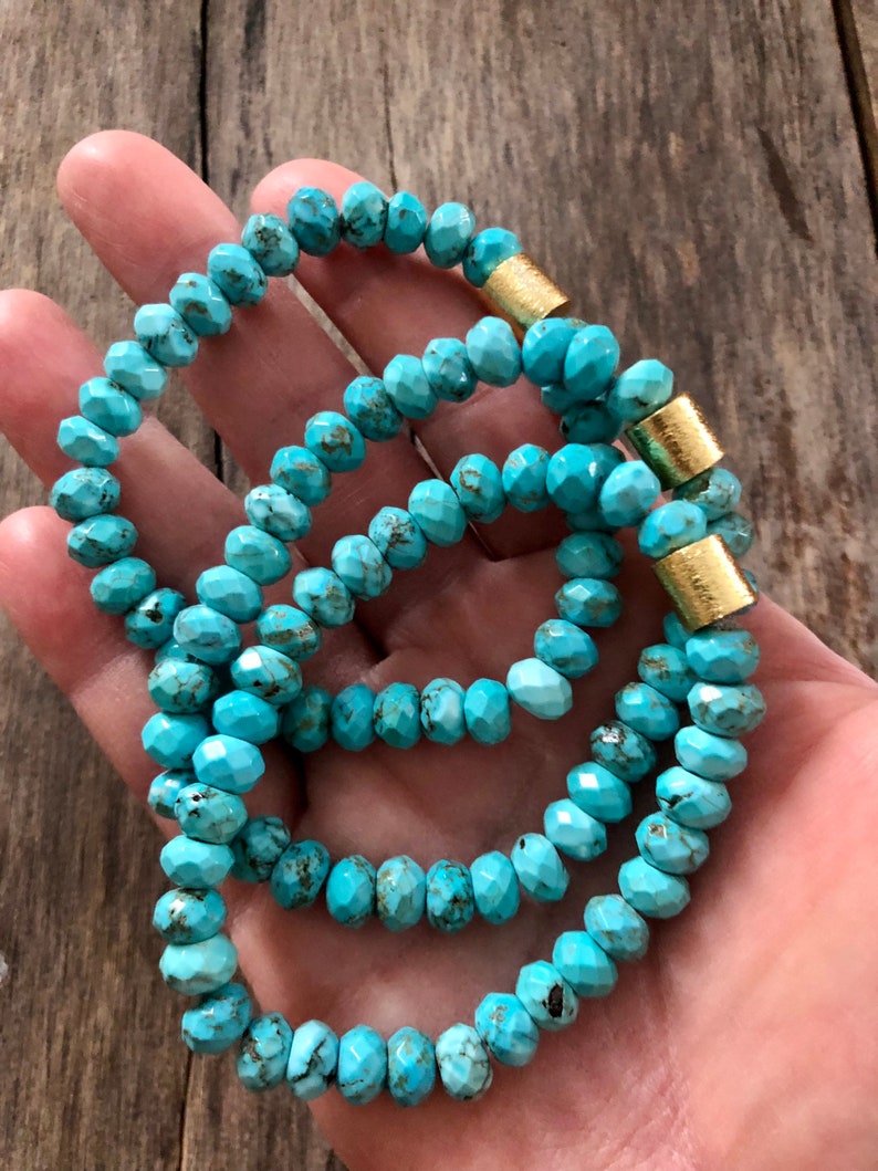 May include: Three turquoise beaded bracelets with gold accents. The beads are faceted and have a slightly irregular shape. The bracelets are stacked on top of each other.