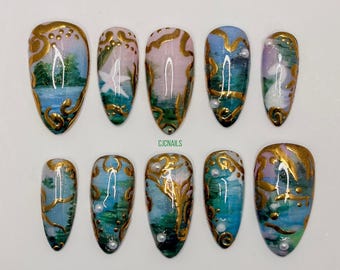 May include: A set of ten press-on nails featuring a hand-painted landscape design in shades of blue, green, and pink, accented with metallic gold swirls and small white pearls. The text CJCNAILS is printed in green in the center.