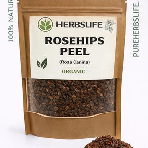 Könnte beinhalten: Ein brauner Papiersack mit einem transparenten Fenster, das Hagebutten-Schalen zeigt. Der Beutel trägt den Text "HERBSLIFE ROSEHIPS PEEL (Rosa Canina) ORGANIC" und "100% NATURAL". Ein kleiner Haufen Hagebutten-Schalen liegt vor dem Beutel.