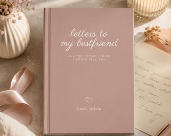 May include: A dusty rose hardcover journal with white text that reads Letters to my bestfriend, ALL THE THINGS I WISH I COULD TELL YOU, a small heart icon, and the text Love, Olivia. The book has a smooth matte finish and a vertical spine.