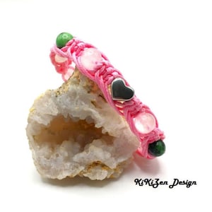 Peut inclure: Bracelet en cordon rose avec des perles roses et vertes et des breloques en forme de cœur argentées.