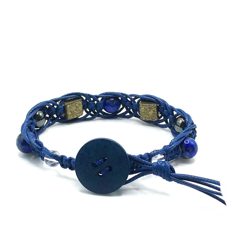 Pode incluir: Um bracelete tran&ccedil;ado azul com fecho de bot&atilde;o azul escuro. O bracelete apresenta contas azuis, douradas e prateadas.