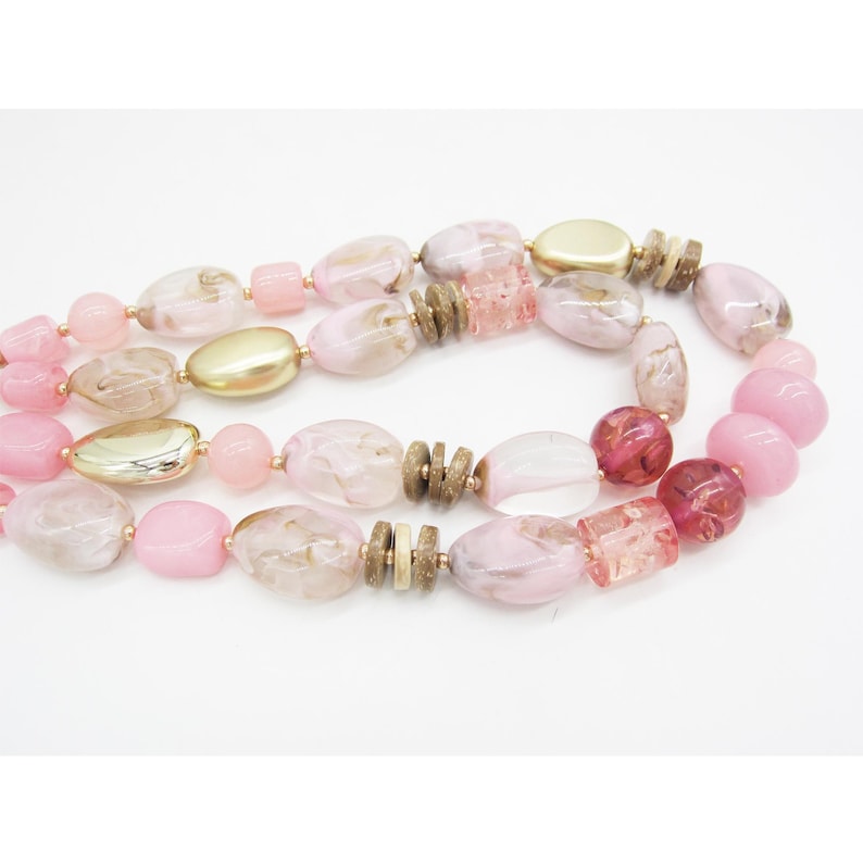 Pu&ograve; includere: Collana a pi&ugrave; fili con perline rosa, oro e marroni. Le perline sono rotonde, ovali e rettangolari. La collana &egrave; presentata su sfondo bianco. Un accessorio di moda.