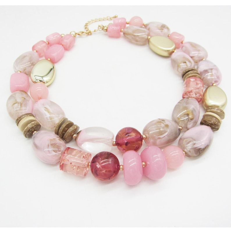 Pu&ograve; includere: Una collana a due fili con un mix di perline rosa, marroni e dorate. La collana presenta perline ovali, rotonde e rettangolari, con una catena e chiusura color oro. Le perline sono in acrilico e legno.