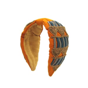 May include: Orange headband with a beaded design featuring blue and gold beads. The headband is made of fabric and has a padded interior.