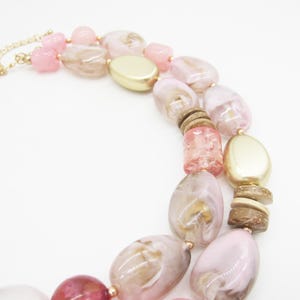 Pu&ograve; includere: Una collana a strati con grandi perline irregolari nei toni del rosa, dell'oro e del marrone. La collana ha una catena color oro e include perline ovali e cilindriche. Il design &egrave; adatto a una variet&agrave; di occasioni.