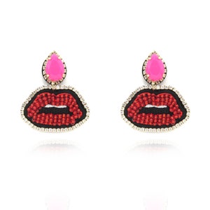 May include: A pair of red beaded lip earrings with pink teardrop-shaped stones. The earrings are made of metal and have a gold finish.