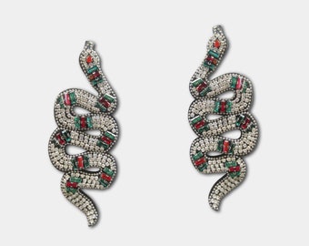 May include: A pair of silver snake earrings with red, green, and white rhinestones.