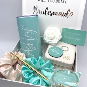 May include: A white gift box with a teal and white tumbler, a teal and white scrunchie, a gold pen, a white card with the text "I can't say I do without you!" and a teal and white jewelry box with a keychain.