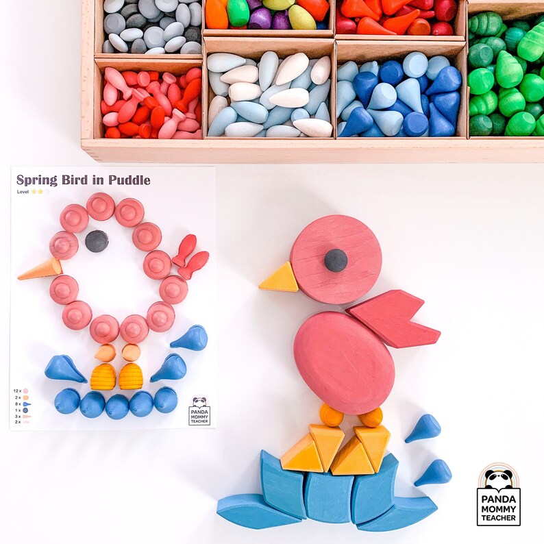May include: A wooden toy bird in pink and red is standing on a blue and yellow wooden puddle. The bird is made of several pieces and the puddle is made of several pieces. The toy is part of a learning activity called "Spring Bird in Puddle".