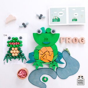 May include: A green wooden frog puzzle with a light blue pond and lily pad. The puzzle pieces are shaped like a frog, lily pad, and water. The frog has a green body, yellow belly, and red eyes. The puzzle is made of wood and is a great educational toy for children.