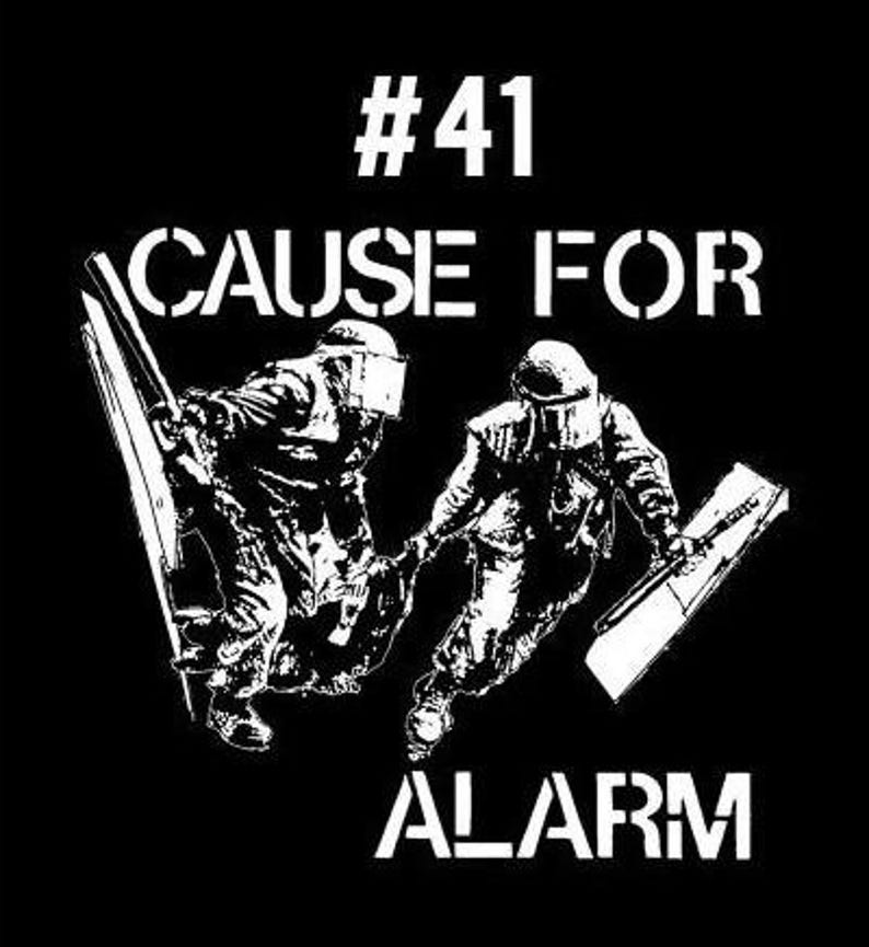 Puede incluir: Dise&ntilde;o gr&aacute;fico en blanco y negro con el texto "#41 CAUSE FOR ALARM" y dos figuras con equipo antidisturbios sosteniendo escudos.