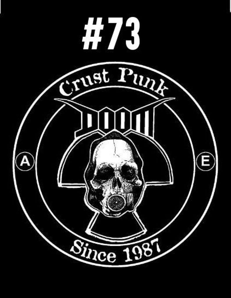 以下が含まれることがあります： ガス マスクをつけた頭蓋骨が描かれた白黒のロゴ。ロゴには「Crust Punk」と「Doom」の文字が書かれており、その下に「#73 Since 1987」の文字が書かれている。