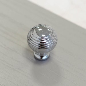 Könnte beinhalten: Ein runder, gerippter Chrom-Schrankknauf.