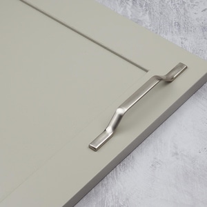 May include: A silver cabinet door handle with a curved design. The handle is mounted on a light gray cabinet door.