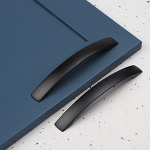 May include: Two black arched cabinet pulls, one on top of the other, on a blue surface.