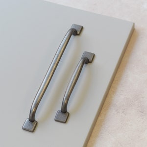 Puede incluir: Dos tiradores de armario de metal plateado con un diseño curvo. El tirador más grande mide aproximadamente 15 cm de largo y el más pequeño aproximadamente 10 cm.