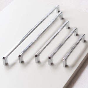 May include: Five silver cabinet pulls of varying lengths. The pulls are rectangular with rounded edges.