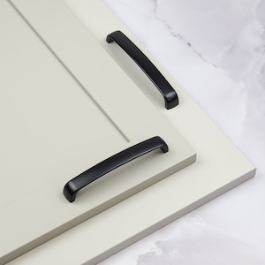 May include: Two black cabinet pulls, one longer than the other, are shown on a white surface. The pulls are made of metal and have a simple, modern design.