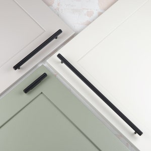 Può includere: Tre maniglie per armadietti nere, ciascuna con una lunghezza diversa, sono mostrate su uno sfondo bianco, verde e grigio chiaro.