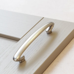 May include: A silver cabinet door handle with a curved design.