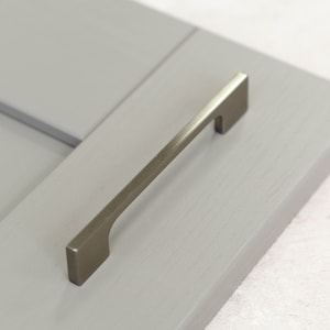 Può includere: Una maniglia per armadio in nichel spazzolato con forma rettangolare e un design leggermente curvo.